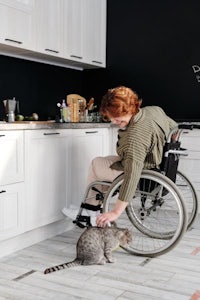 a woman in a wheelchair is petting her cat in the kitchen