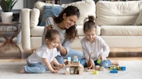 a mother and two children playing with wooden blocks in a living room